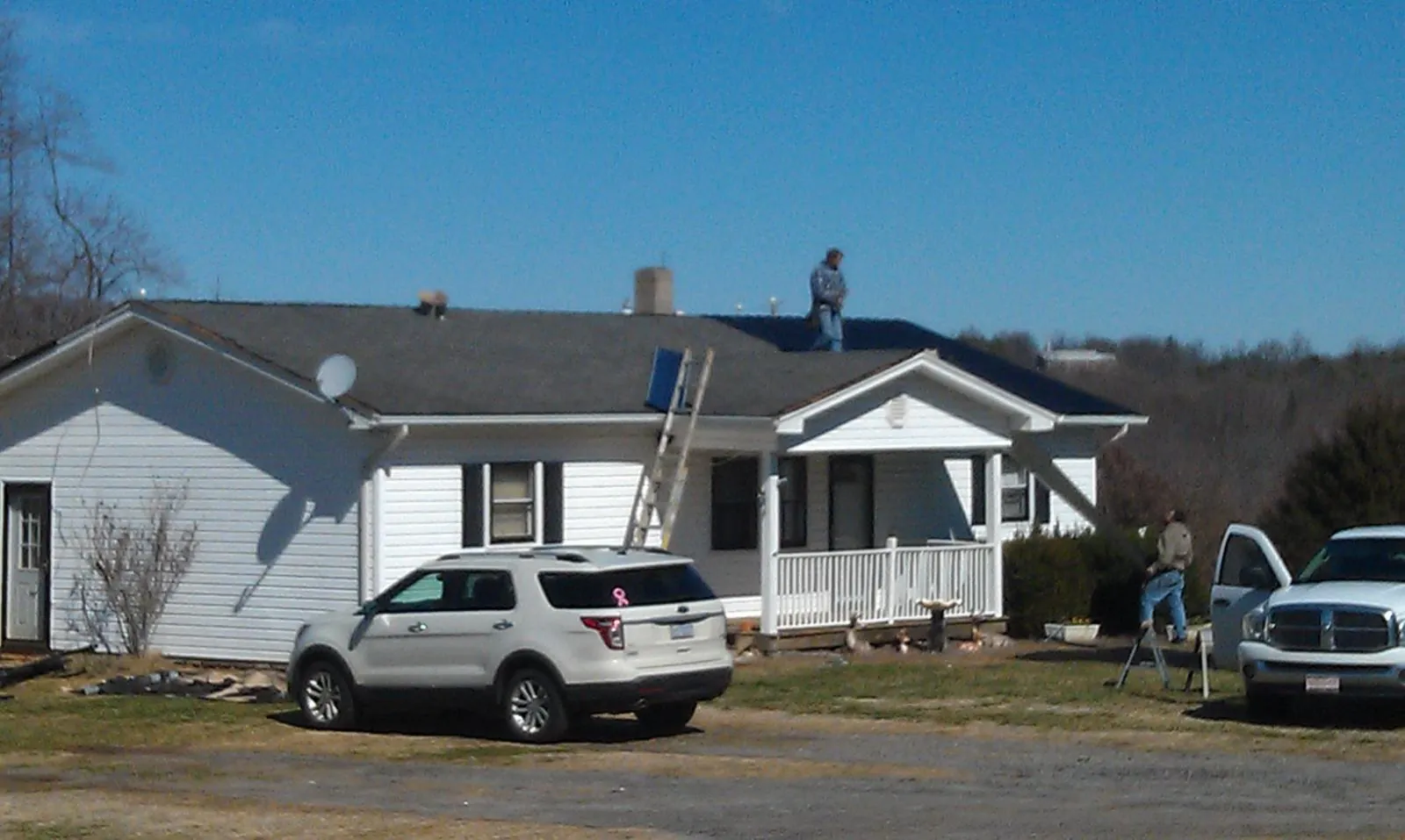 Roofers stripping shingles from a white ranch house roof in Geneseo